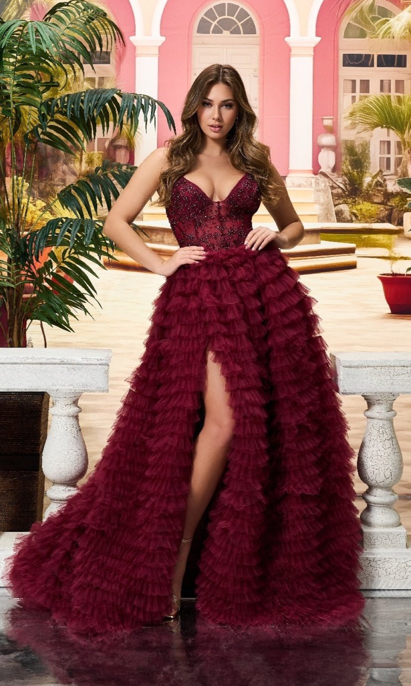 A woman poses outdoors in the Colette CL8330 long prom dress, featuring a burgundy ruffled skirt with a high slit and a sheer embroidered bodice.